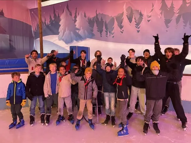 Een grote groep leden juicht met de armen omhoog op een overdekte schaatsbaan met winters decor.