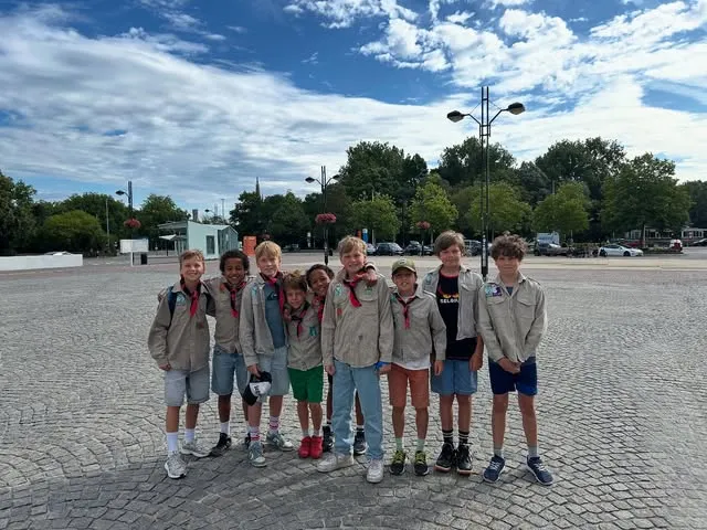 Een groep jongens in scoutsuniform met rode das poseert samen op een groot plein.