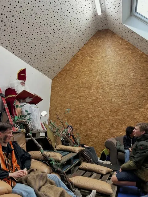 Sinterklaas leest voor uit zijn boek terwijl leden er ontspannen naar luisteren.